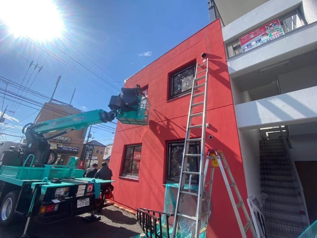 店舗建物の2面に渡り照明入りサイン看板の大型フレームを高所作業で安全に取り付ける様子